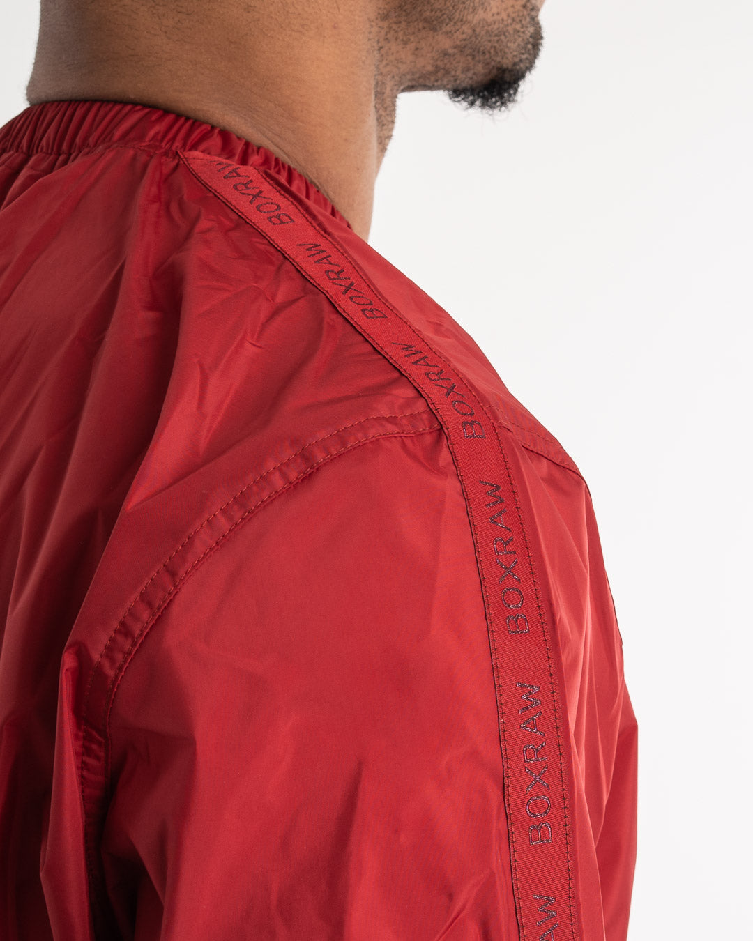 Man in a red sauna suit tracksuit with a white boxraw logo on the chest as well as adjustable wrist straps and made from polyester.